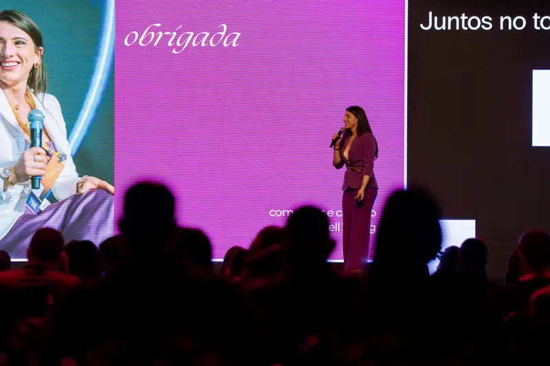 Bell no palco diante do público em um telão lilás.